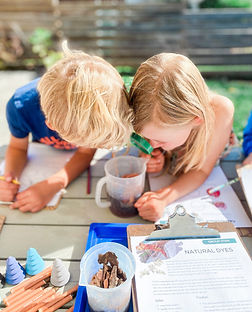 Children exploring science in nature using a magnifying glass during hands-on forest school activity.
